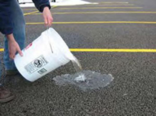 Person pouring a bucket of water on a porous parking lot